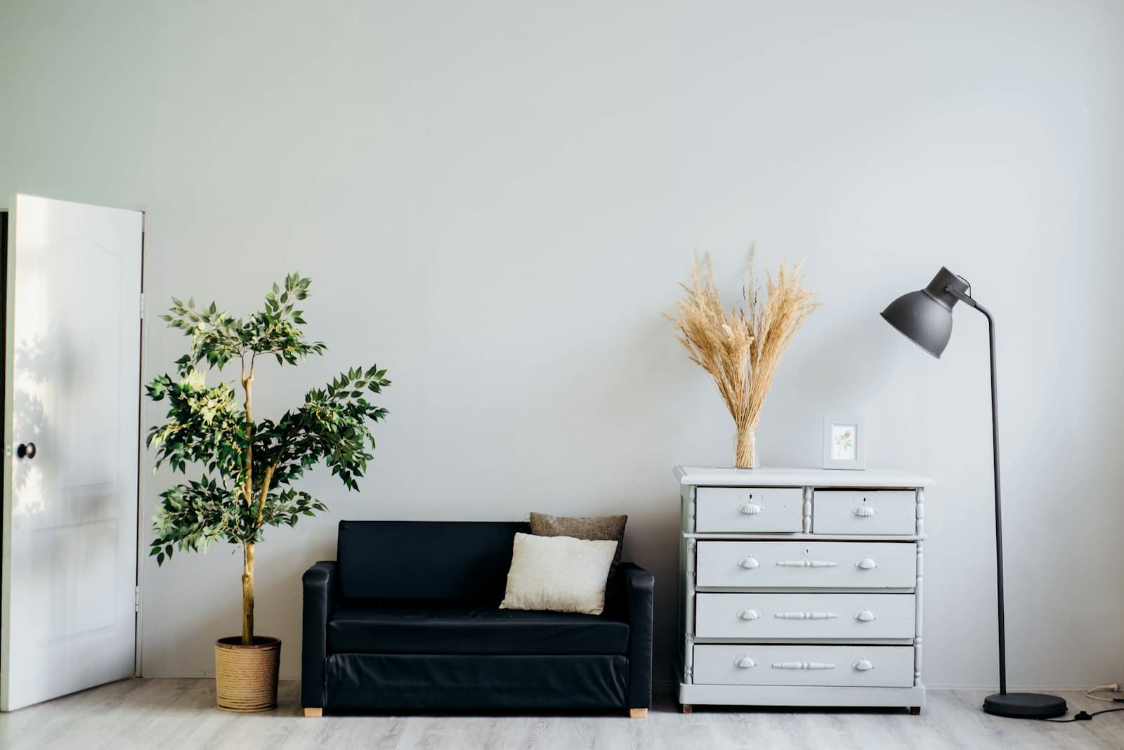 Sofá negro, cómoda gris y lámpara de pie junto a una pared clara en un interior neutro